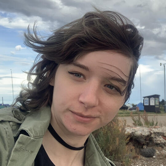 A photograph of Errol Seymour, a person with dark, chin-length hair, red lipstick, and big mirrored sunglasses.