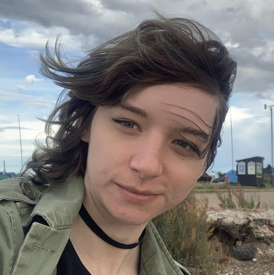 A photograph of Errol Seymour, a person with dark, chin-length hair, red lipstick, and big mirrored sunglasses.